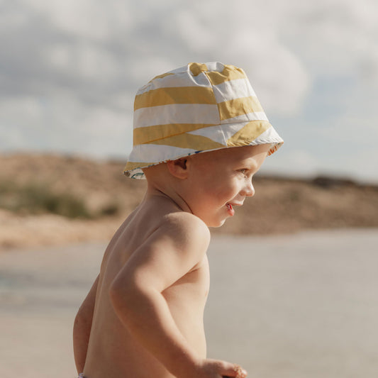 child wearing the little dutch reversible bucket hat in honey stripe on the beach