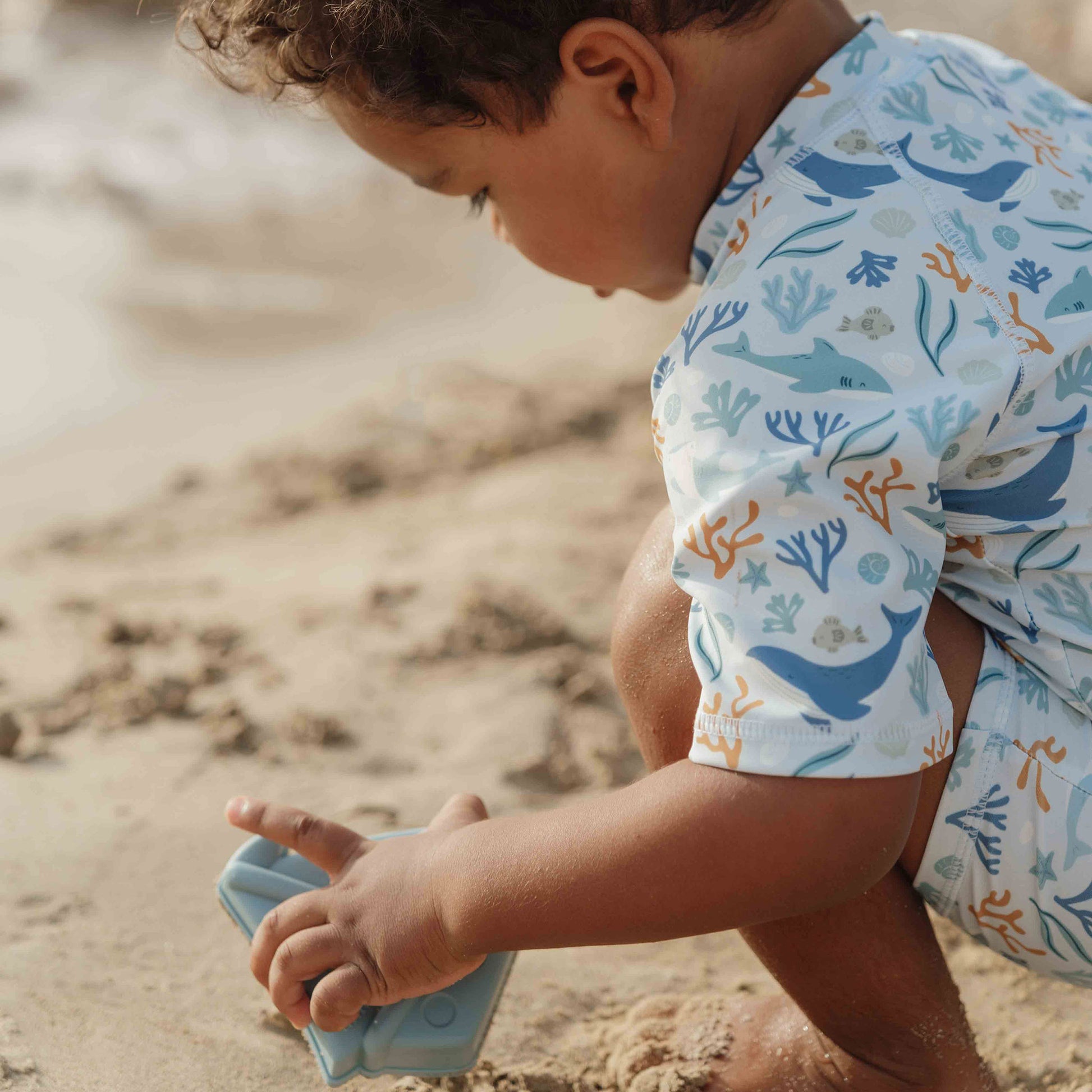 Close Up Little Boy Wearing The Little Dutch Short Sleeved Swimsuit In Ocean Dreams Blue