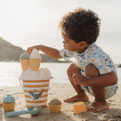 Little Boy Wearing The Little Dutch Short Sleeved Swimsuit In Ocean Dreams Blue & Playing Wiith The Little Dutch Ice Cream Bucket Set